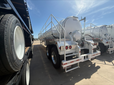 Vacuum trailer rear view showing cylindrical tank and dual axles with rear lights and railing, under clear sky