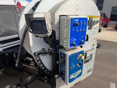 Kenworth T470 Vactor truck vacuum system control panel and drum housing showing blue control boxes with knobs, gauges, and warning labels.