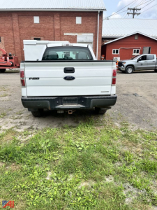 Ford F-150 tailgate view showing 3.5L badge and rear bumper with hitch in a used pickup truck lot.