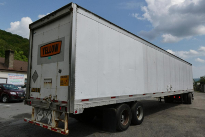 Great Dane trailer showing side and rear with yellow hazard sign and rear doors, dual axles, white body, and yellow warning placard.