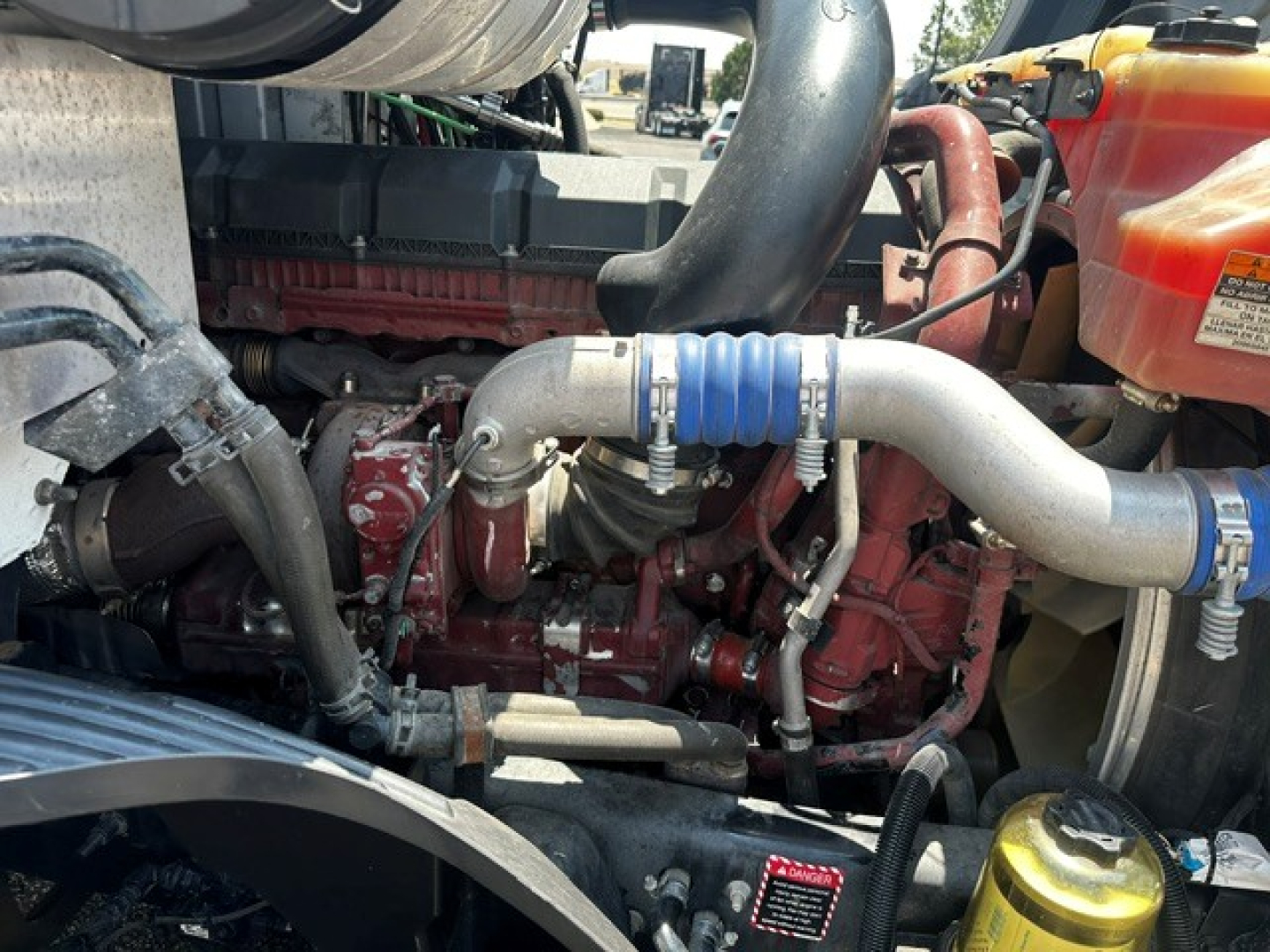 Mack ANTHEM engine bay showing coolant reservoir hose clamps and intake piping in red engine compartment.