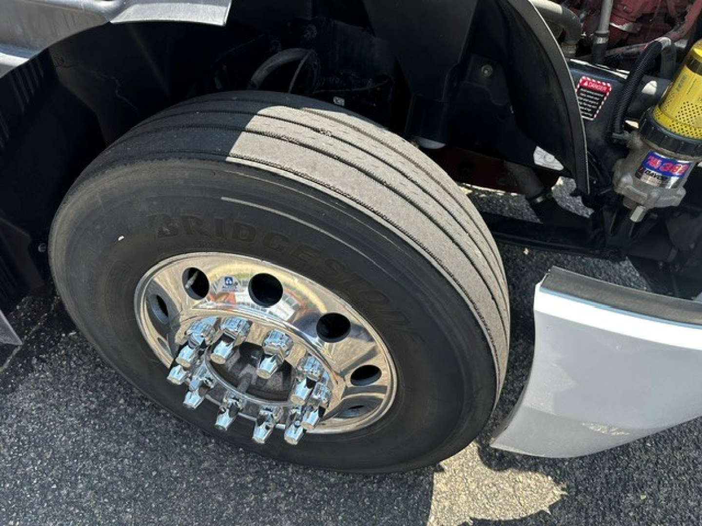 Front wheel close-up of a Mack Anthem truck showing Bridgestone tire and chrome dual-stack lug nuts; part of the front fender and suspension visible.