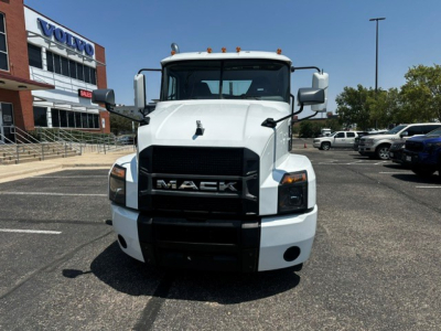 Front view of a white 2021 Mack Anthem conventional daycab truck with black grille and large bumper, showroom at a truck dealer in background.