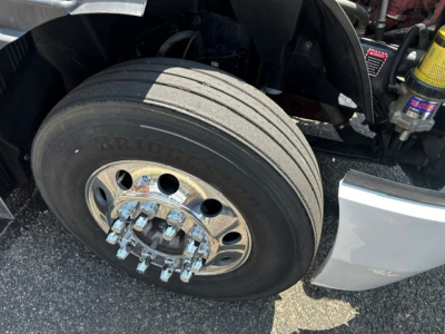 Front wheel close-up of a Mack Anthem truck showing Bridgestone tire and chrome dual-stack lug nuts; part of the front fender and suspension visible.