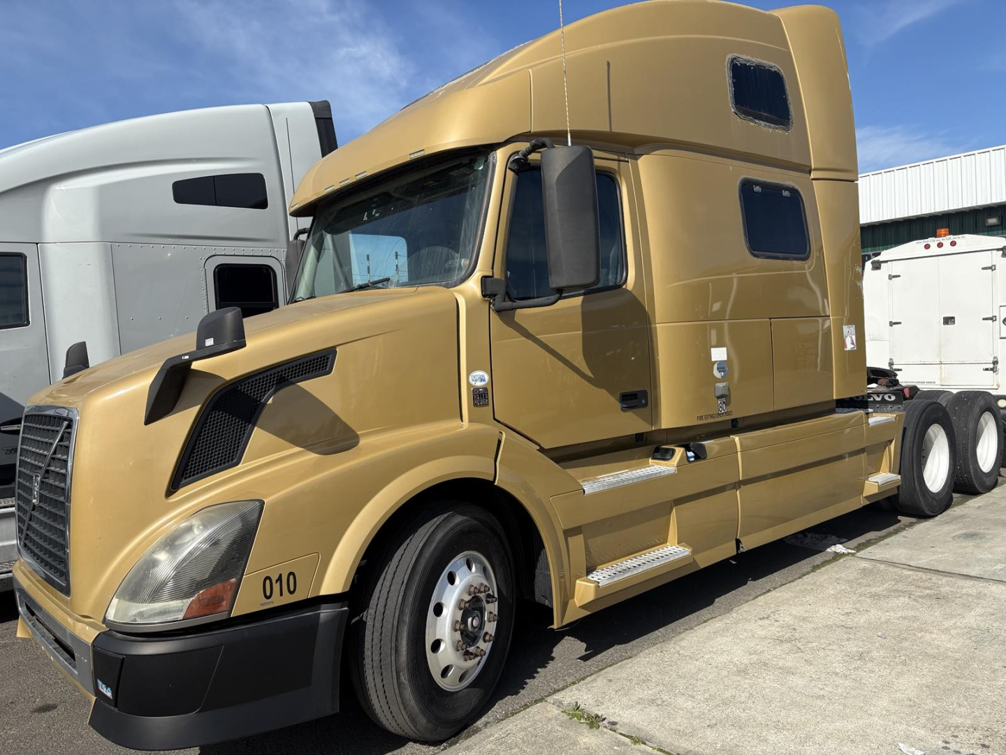 Volvo 770 conventional sleeper truck in tan color showing cab and front bumper with wheel, side mirrors, and sleeper area.