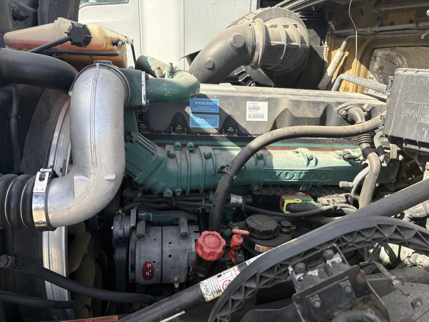 Volvo engine bay showing green Volvo engine with hoses, red oil cap, and various components in a conventional sleeper truck.