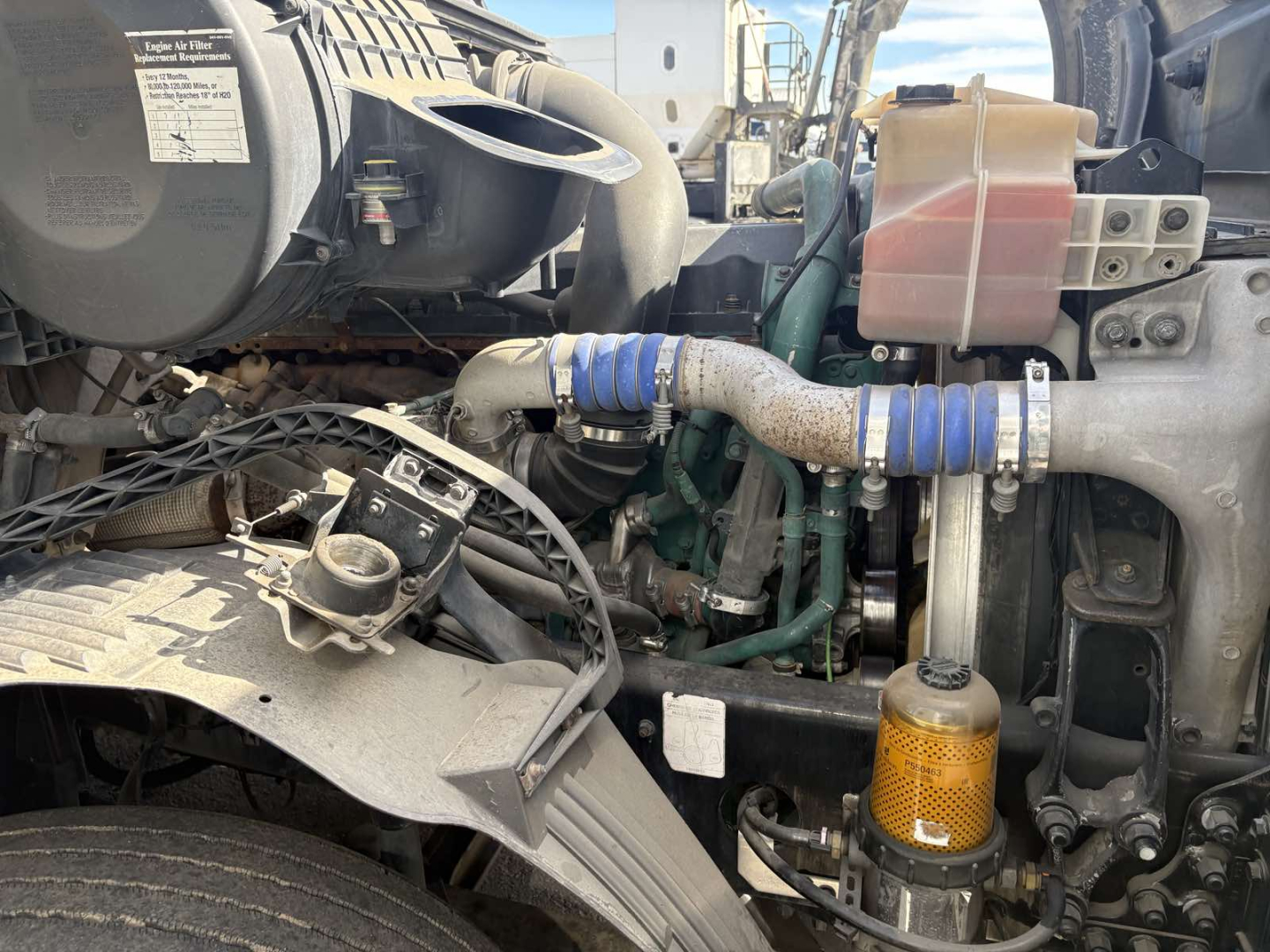 Volvo engine bay showing coolant reservoir, blue hose clamps, and various engine components in the front of a 2013 Volvo 770 conventional sleeper truck.