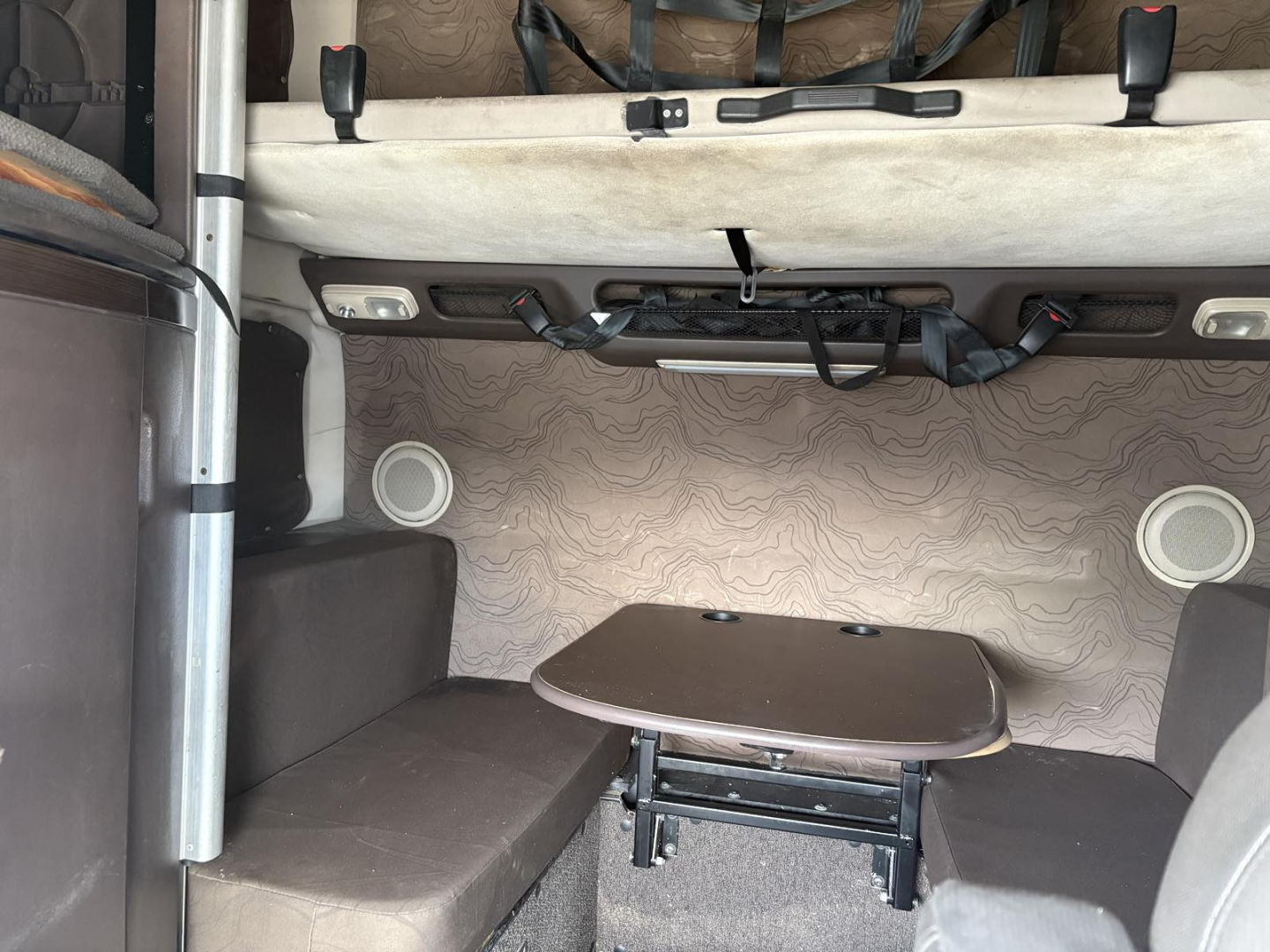 Volvo 770 sleeper cab interior showing seating area with table and bed area, cabin walls with light patterned upholstery, and overhead storage straps.