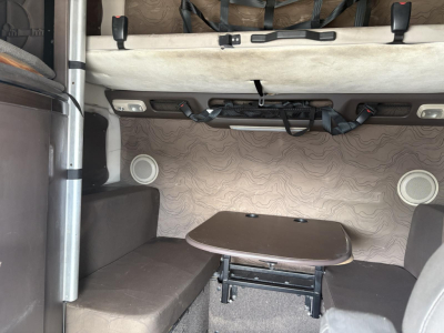 Volvo 770 sleeper cab interior showing seating area with table and bed area, cabin walls with light patterned upholstery, and overhead storage straps.