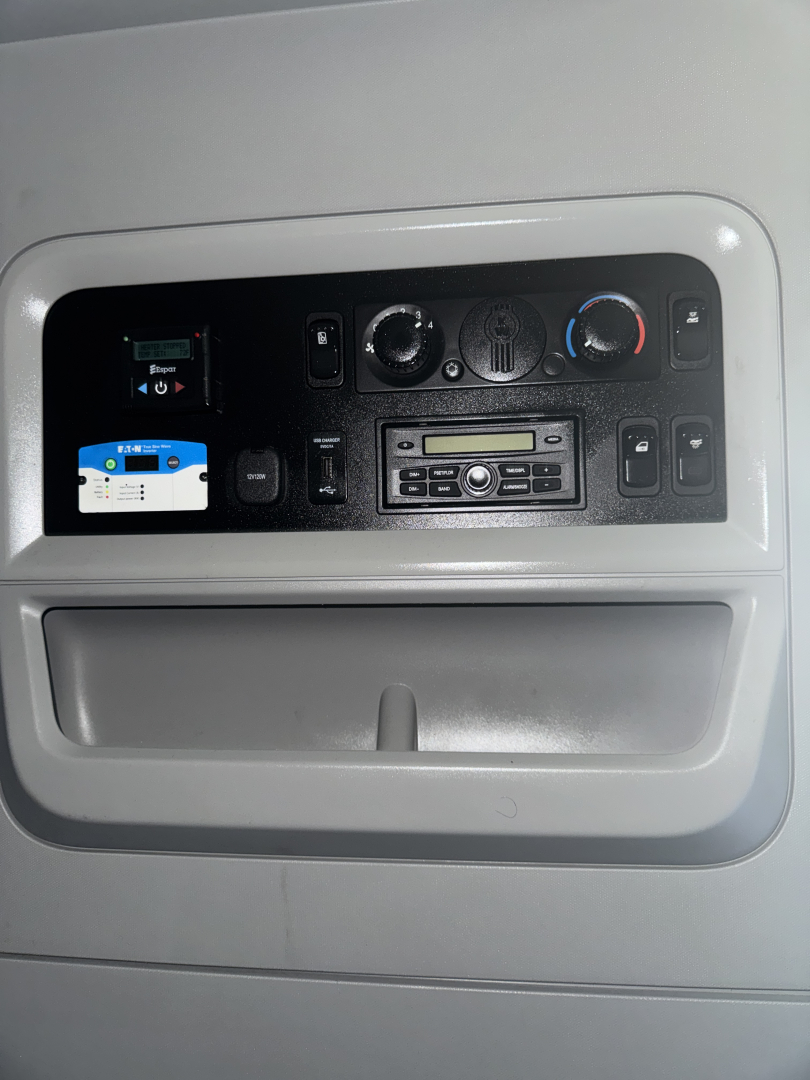 Dashboard panel of a Kenworth truck showing air conditioning controls, radio, and a small screen with a blue and white interface.