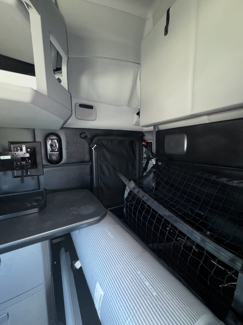 Kenworth T680 cab interior showing sleeper area and storage nets with light grey upholstery and control panel.