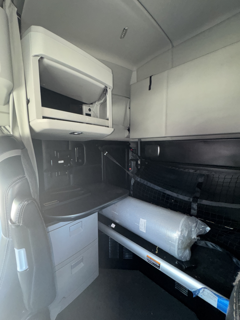 Kenworth T680 cabin interior showing sleeper area with storage compartments, rolled mats, and overhead shelf.