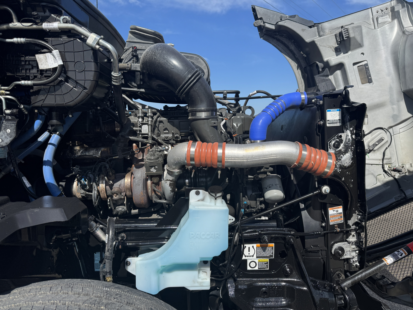 Kenworth T680 engine bay with blue coolant reservoir, turbocharger, hoses, and radiator components visible.