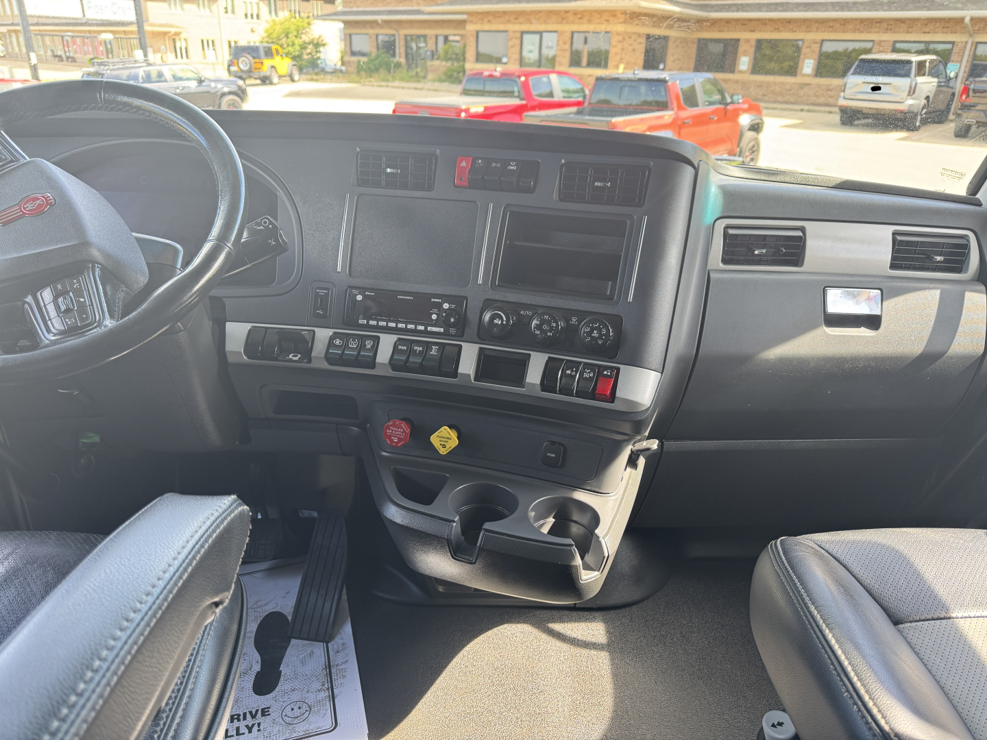 Kenworth T680 truck interior dashboard and steering wheel view showing center console, cup holders, and control panels.