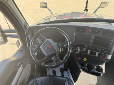 Kenworth T680 cabin interior showing steering wheel and dashboard with multiple gauges and control panels.