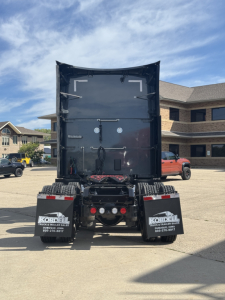 Rear view of a Kenworth T680 truck tractor in a dealership lot showing the back of the trailer/box with mudflaps and hitch area.