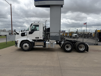 White Mack AN64T highway tractor side view showing front cab, dual rear axles, fuel tanks, and chassis beneath a dealership sign.