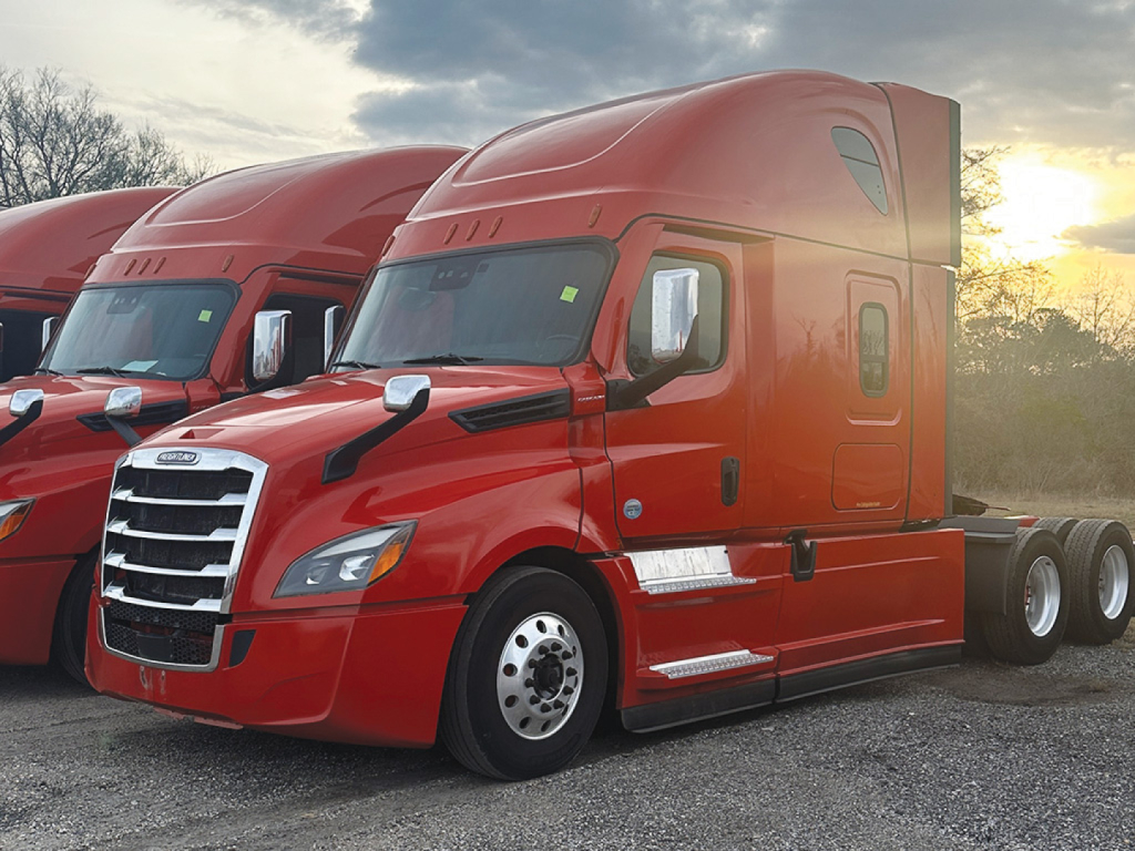 Truck image: red Freightliner Cascadia126 conventional sleeper, side view showing chrome grille, aerodynamic cab, dual rear axles, daytime sun.