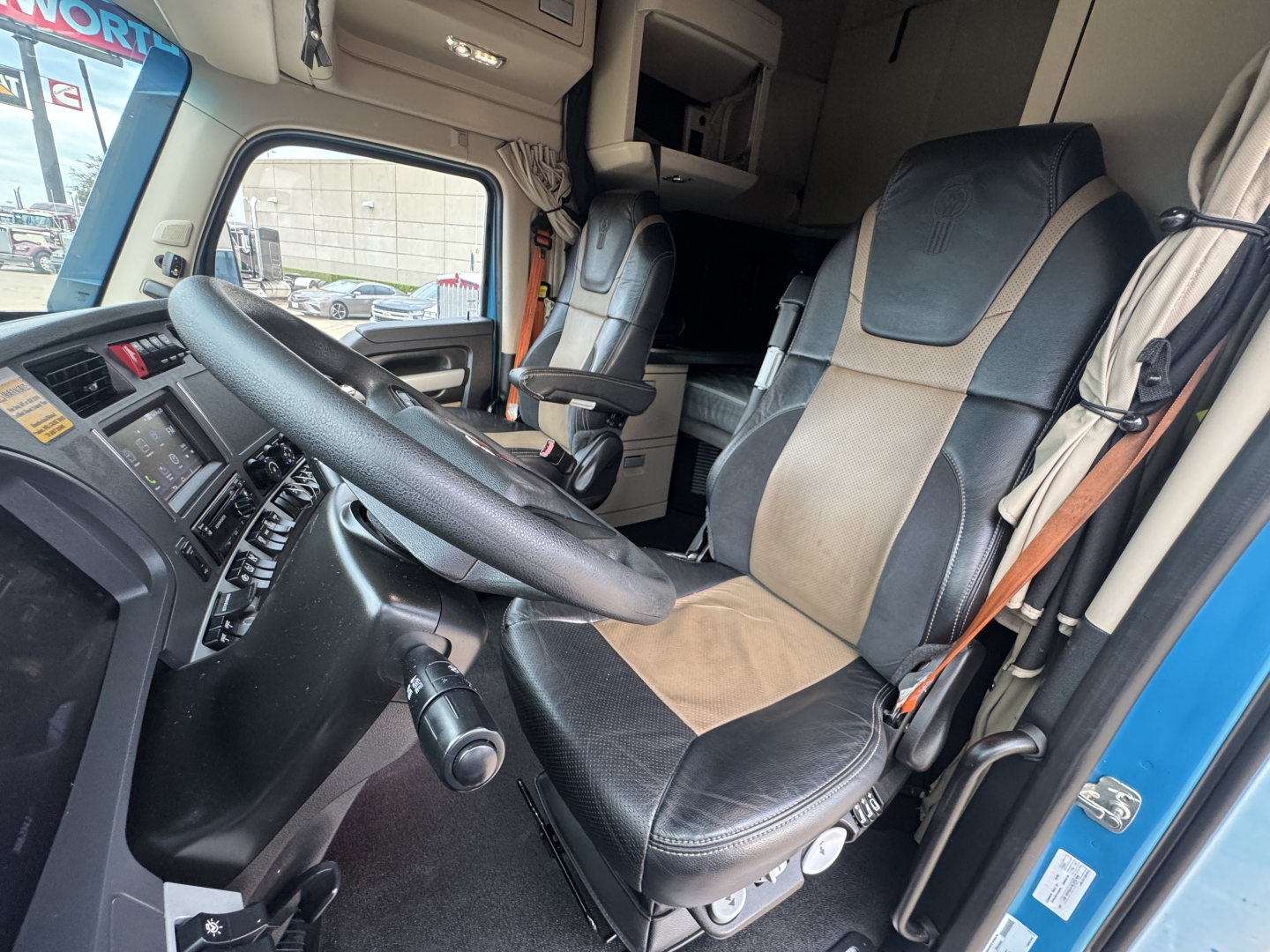 Truck cab interior showing steering wheel, driver's seat and dashboard of a 2024 Kenworth T680. Visible controls and seating area.