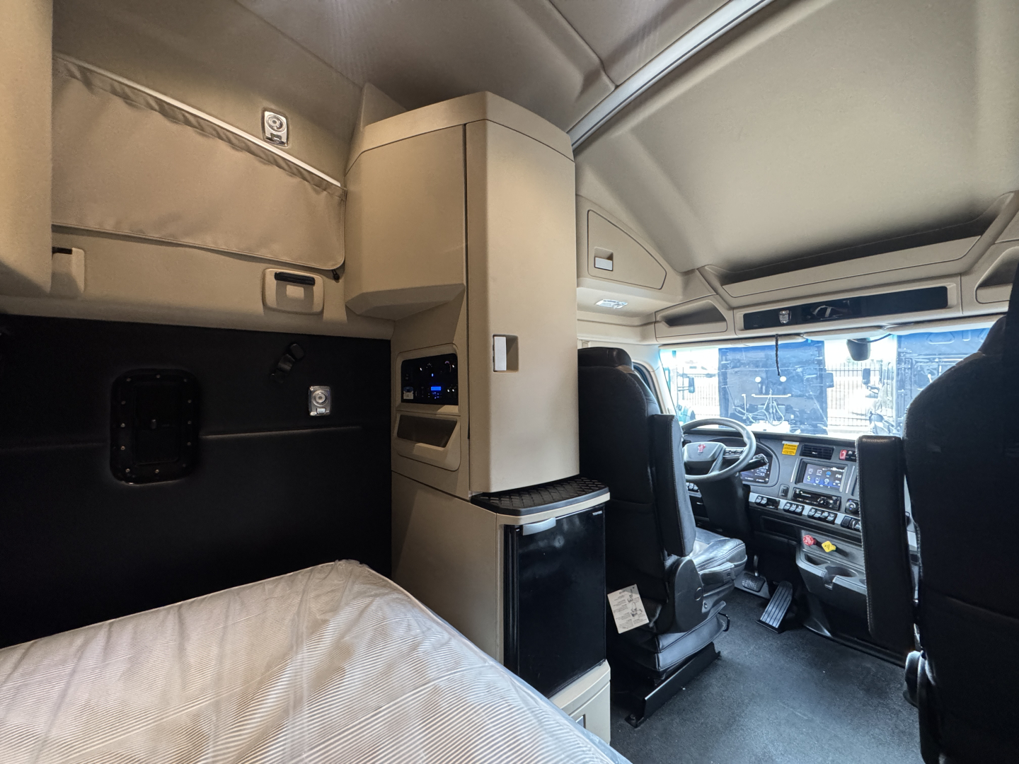 Kenworth T680 sleeper cab interior showing driver's seat, dashboard, center console, and overhead storage compartments.