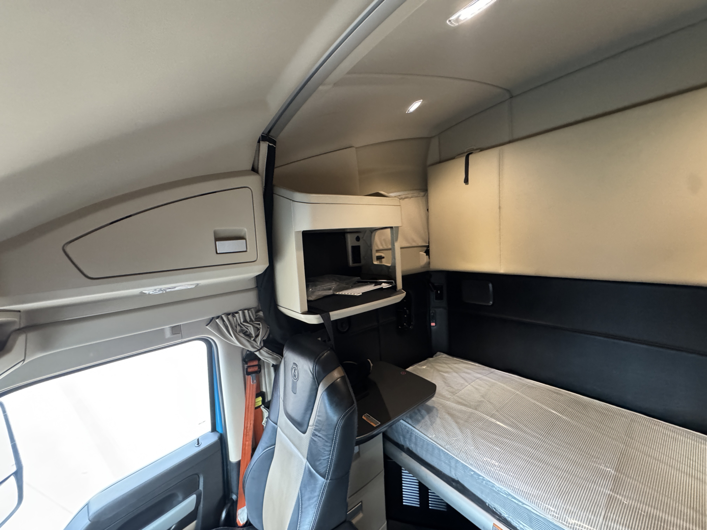 Kenworth T680 cab interior showing sleepers bunk with overhead storage and small work desk area.