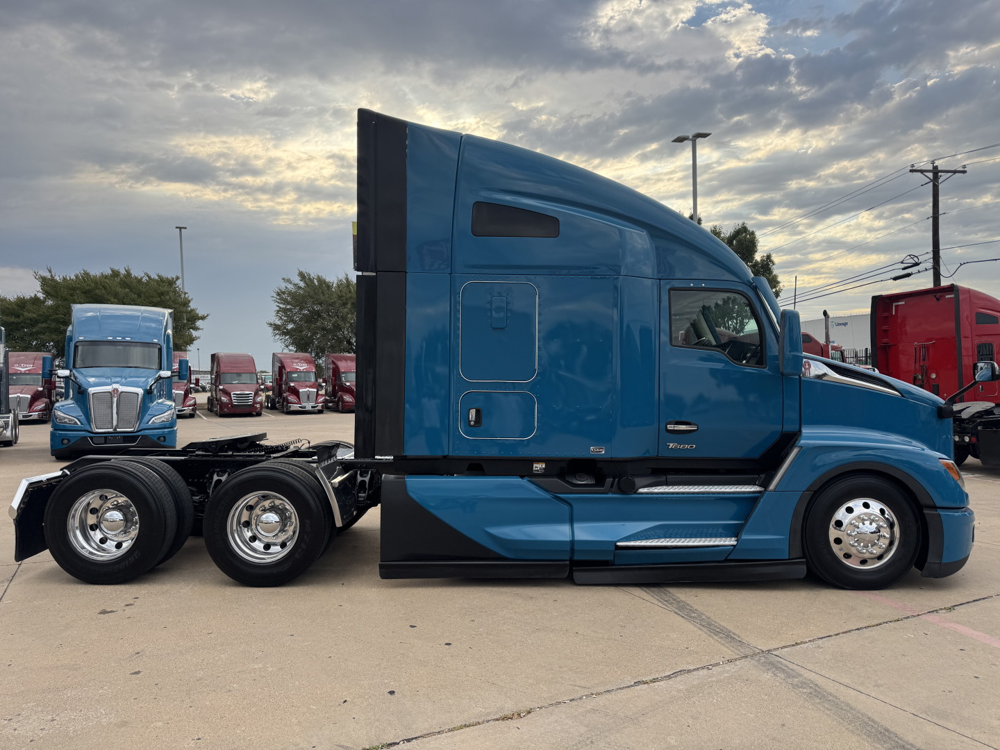 Blue Kenworth T680 tractor in profile view showing sleeper cab, side fuel tanks, and dual rear axles with polished rims.