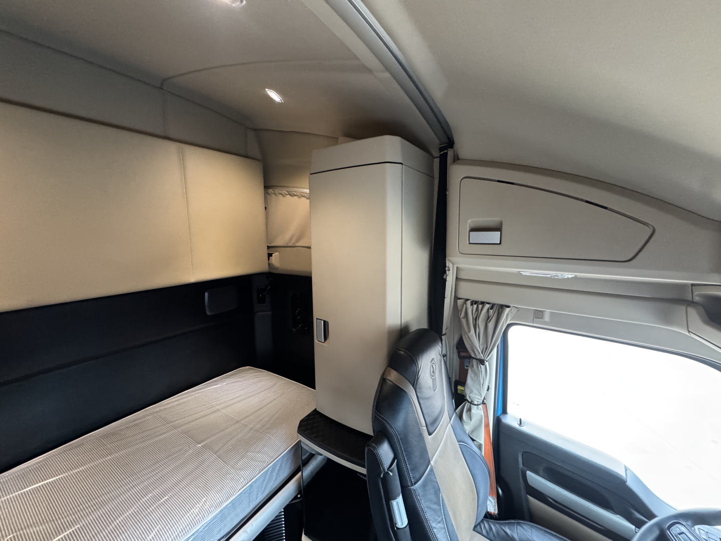 Kenworth T680 sleeper cab interior showing bunk bed with storage cabinet and driver's seat in view.