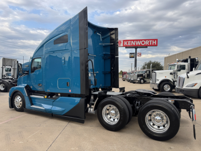 Kenworth T680 truck side profile showing blue cab and rear chassis with dual rear axles in a dealership lot.