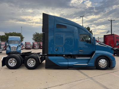 Blue Kenworth T680 tractor in profile view showing sleeper cab, side fuel tanks, and dual rear axles with polished rims.
