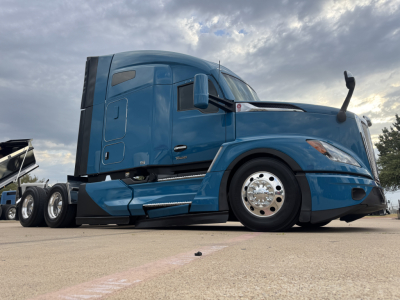 Kenworth T680 tractor cab side view showing blue exterior, sleeper cab, dual rear axles, front fender, and chrome wheels.