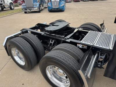 Kenworth T680 tractor chassis showing dual rear axles and fifth wheel, with exposed frame and suspension; chrome wheels and tires visible.