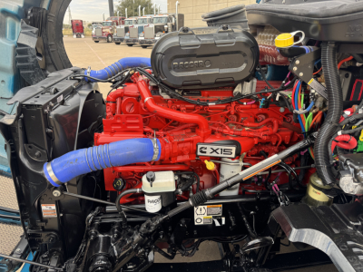 Kenworth T680 engine bay showing red X15 engine with blue coolant hoses and various wiring harnesses.
