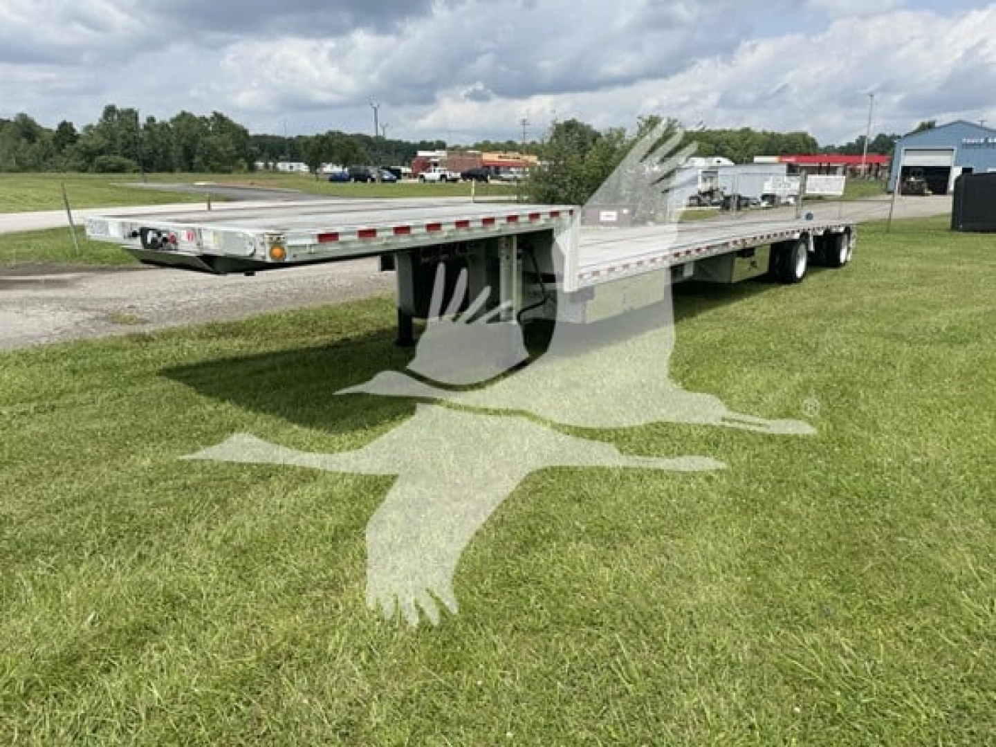 Dropdeck trailer with flatbed platform showing low-angle view, aluminum deck, reflectors along side, and dual rear axles in a grassy lot.