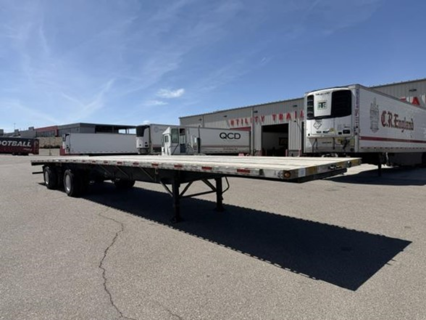 Flatbed trailer with air ride combo, long trailer deck, located in a lot with other trailers; shows a low-angle view of the trailer frame and landing gear.