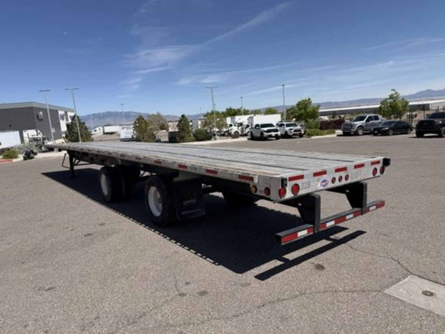 Flatbed trailer showing aluminum deck and dual rear axles with lights and safety rails.