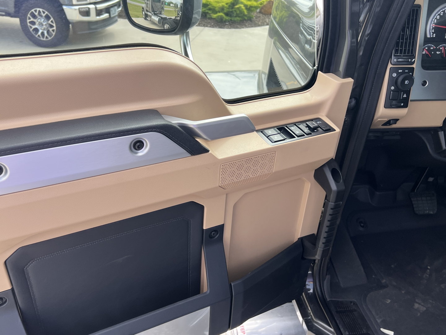 Truck cab interior door panel with power window buttons and beige/gray trim; door pocket and speaker grille visible; steering column area seen in background.