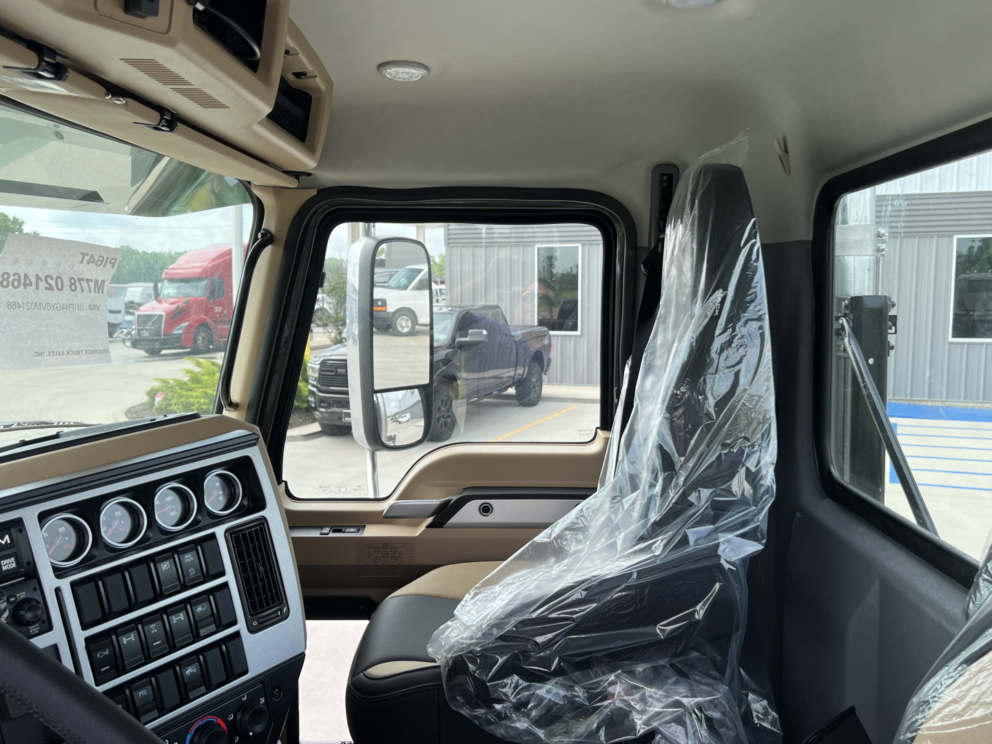 Cab interior of a 2027 Mack PI64T truck showing steering area, instrument cluster, and plastic-covered seat.