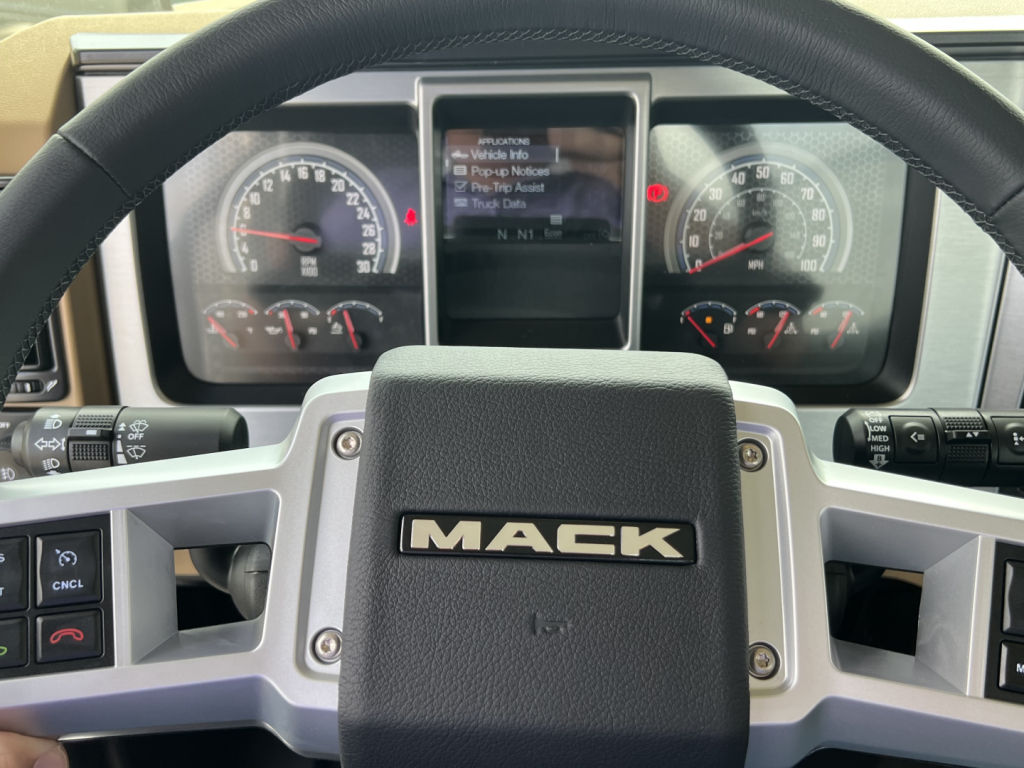 Mack PI64T truck steering wheel and dashboard with Mack logo center; instrument clusters visible with gauges.