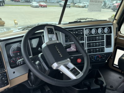 Mack PI64T dashboard and steering wheel in cab showing gauges, controls, and gear selector.  "MACK" logo on steering wheel; visible instrument cluster and dashboard switches.