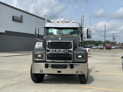 Front view of a new 2027 Mack PI64T conventional daycab truck with chrome bumper, large grille, and Mack emblem; visible windshield, headlights, and hood ornament; dealership lot in background.
