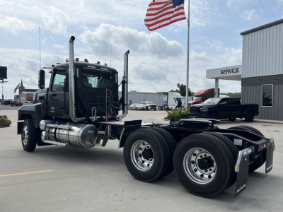 Mack PI64T truck cab and chassis in a dealership lot with dual rear axles and American flag in background.