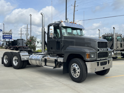 2027 Mack PI64T conventional daycab truck in a dealership lot, front half visible with dual rear wheels and chrome fuel tanks; Mack logo on grille; exhaust stacks and side mirrors visible.