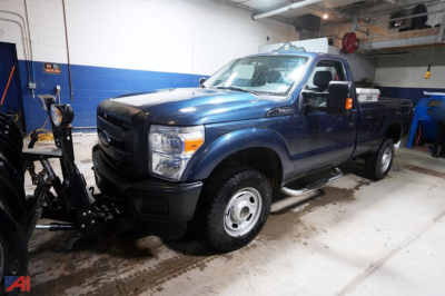 2015 Ford F-250 SD XL pickup truck with plow in a workshop, blue body, extended cab, front grille, large side mirrors, and running boards visible.