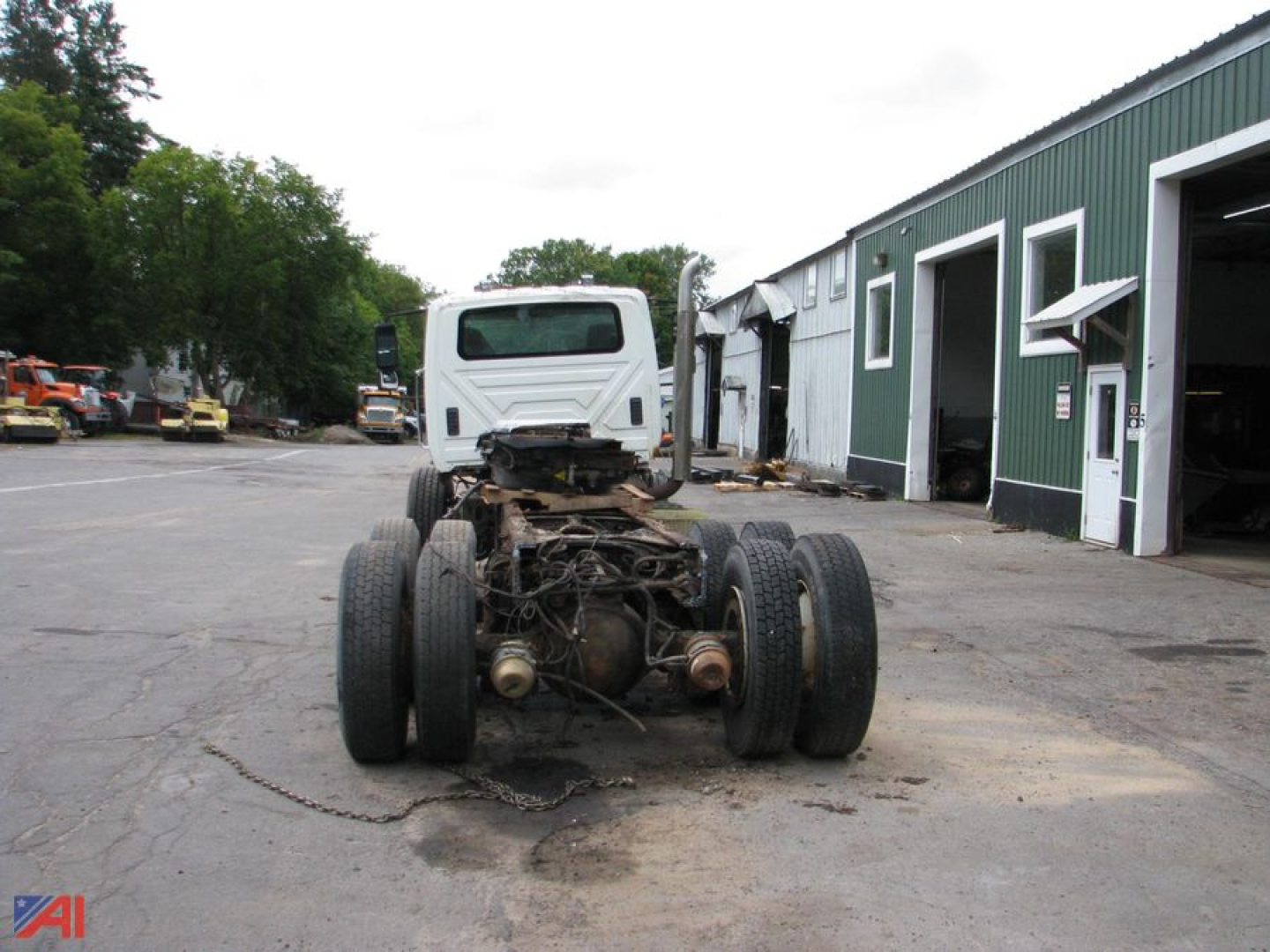 Front view of a used 2013 International SF667 WorkStar 7600 cab and chassis chassis showing rear axle and drive train with dual rear axles, white cab, and industrial lot.