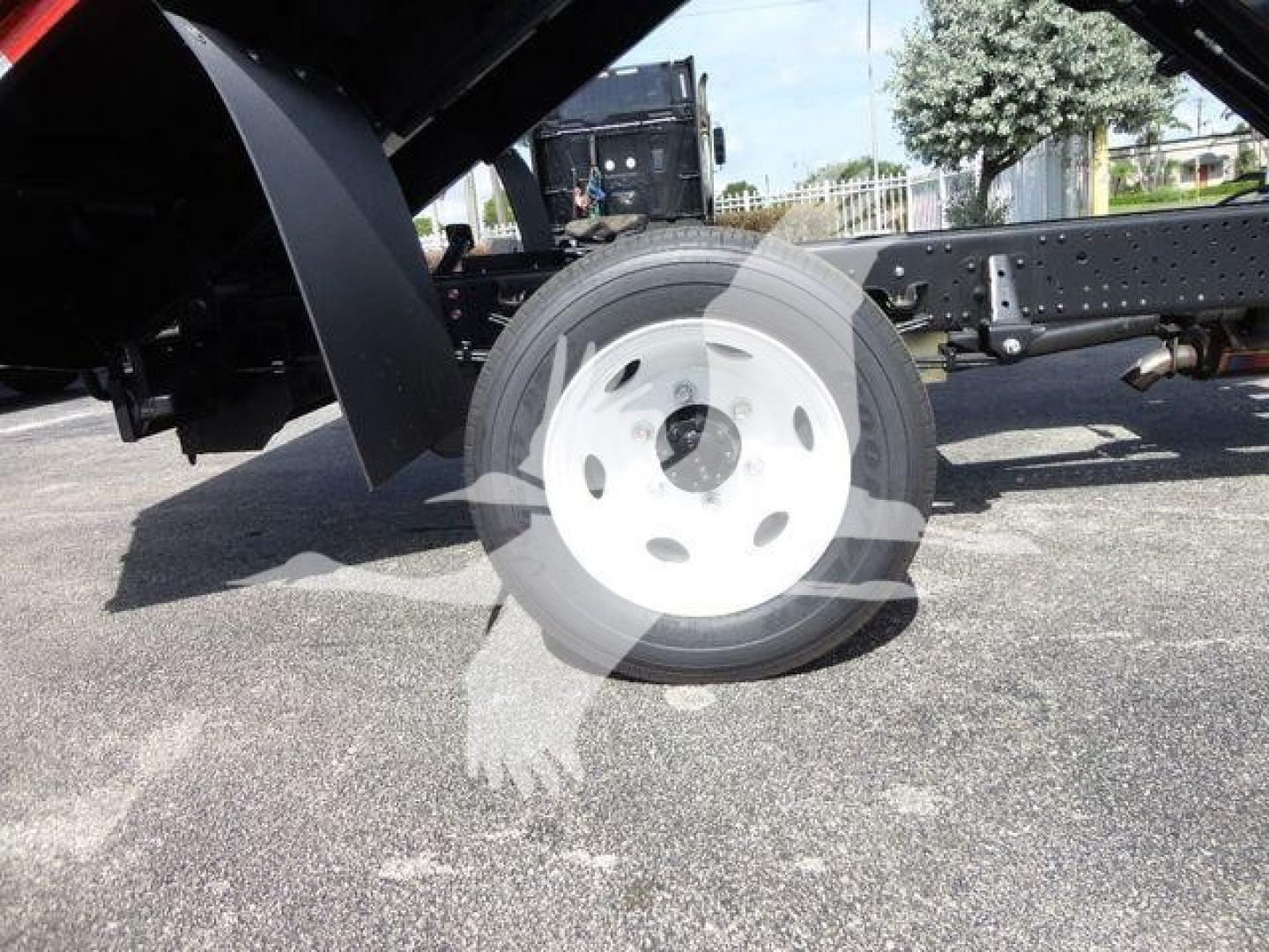 Front wheel and undercarriage of a 2024 Isuzu NPR HD dump truck showing single front axle with white wheel and black chassis
