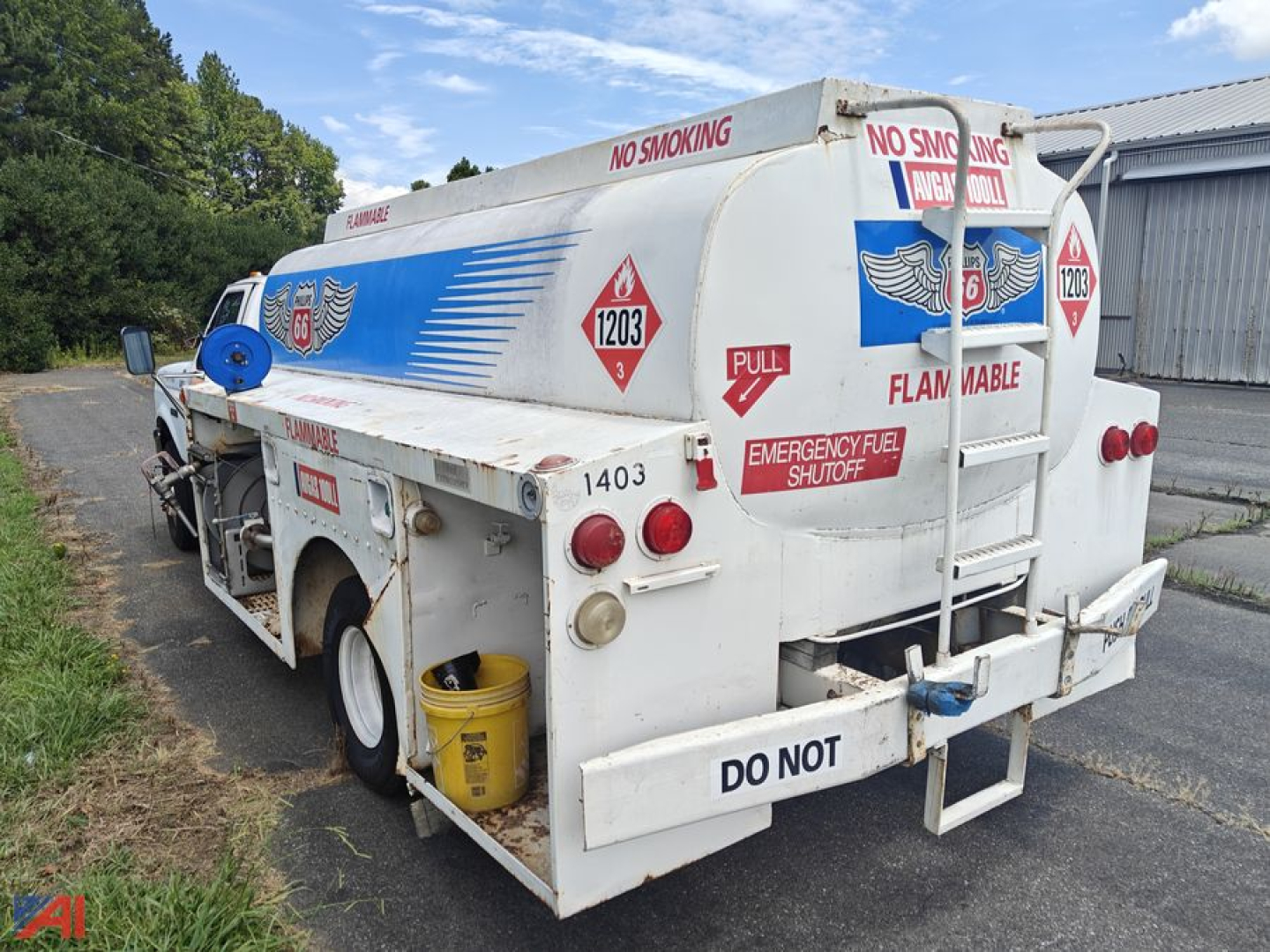 Tank truck rear left view showing hazardous material placards and 'DO NOT' text on bumper, 'No Smoking' signs, and emergency fuel shutoff label.