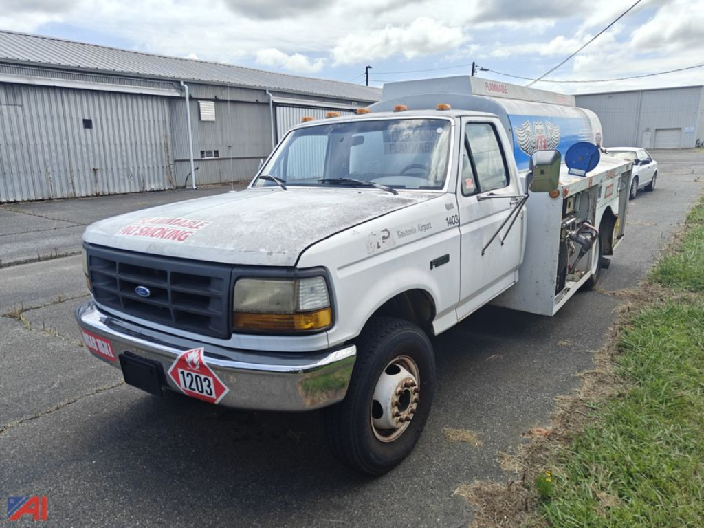 Ford F-Series Super Duty tanker tow truck with white cab and tank body, front view showing warning placards and equipment on side