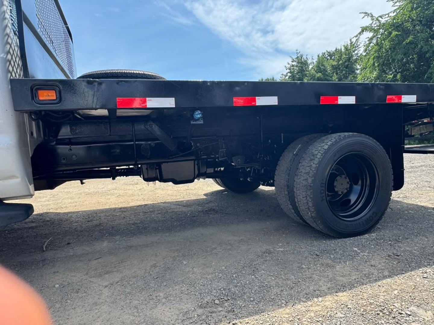 Ford F-550 flatbed truck side view showing wheel, flatbed railing, and reflective hazard stripes.