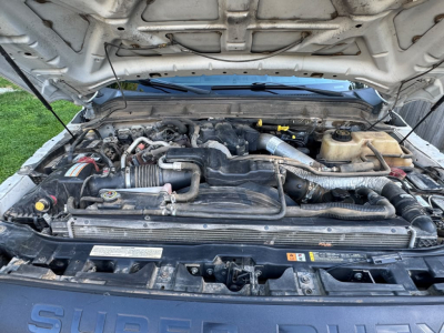 Ford F-550 engine bay showing V8/V10 engine with hoses and battery; visible labels on front radiator support and coolant reservoir.