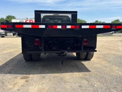 Flatbed tow truck rear view showing flatbed with red/white reflective tape and taillights, hitch, and dual rear wheels.